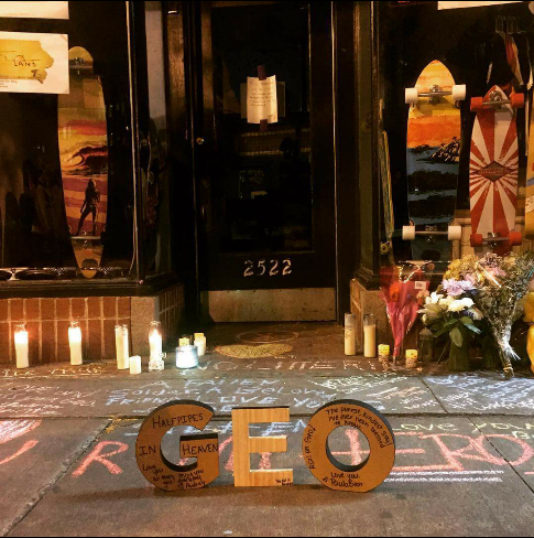 Candles & flowers outside Georgie's store with "GEO" in wooden letters and chalked messages on the sidewalk