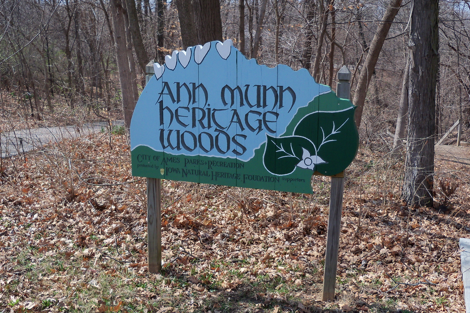 Sign stating "Ann Munn Heritage Woods. City of Ames Parks & Recreation. Protected by Iowa Natural Heritage Foundation supporters"