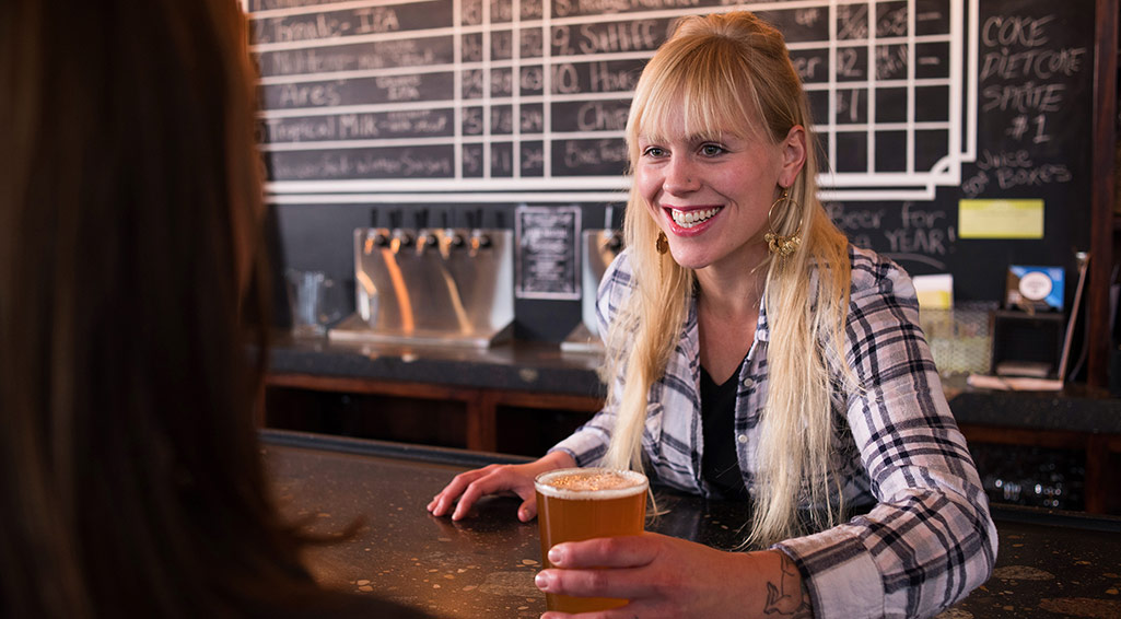 Woman serving a customer a craft beer at a bar counter.